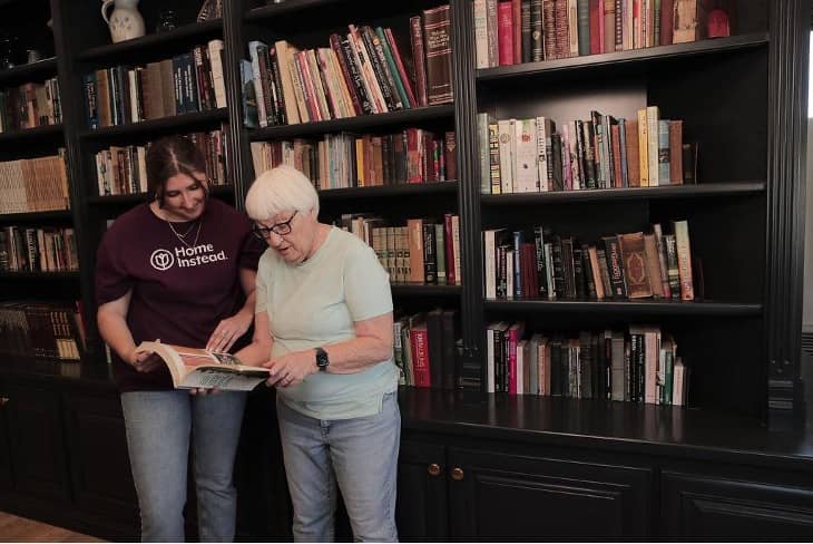 Photo of a Home Instead Care Pro and an Elder Care client looking at an open book in a library