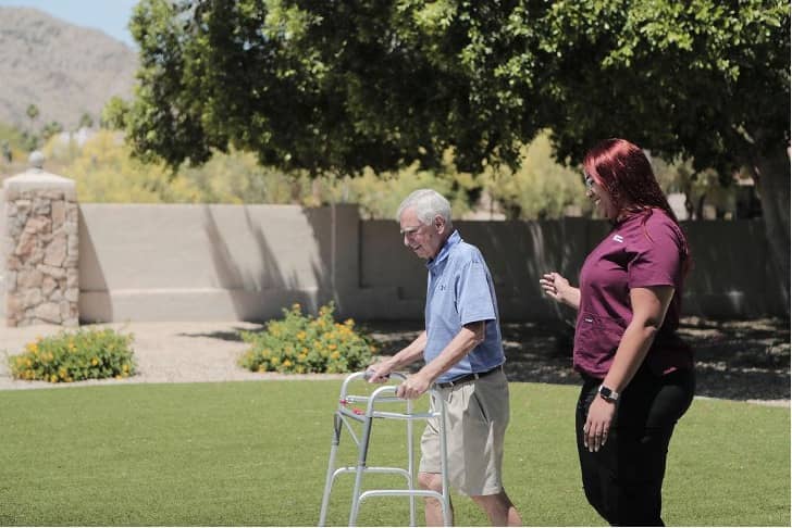 Photo of a Care Professional and an Elder Care client with a walker taking a stroll in a garden