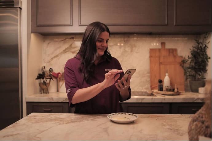 Photo of a Home Instead Care Pro standing at a kitchen island making a schedule on a smart phone.