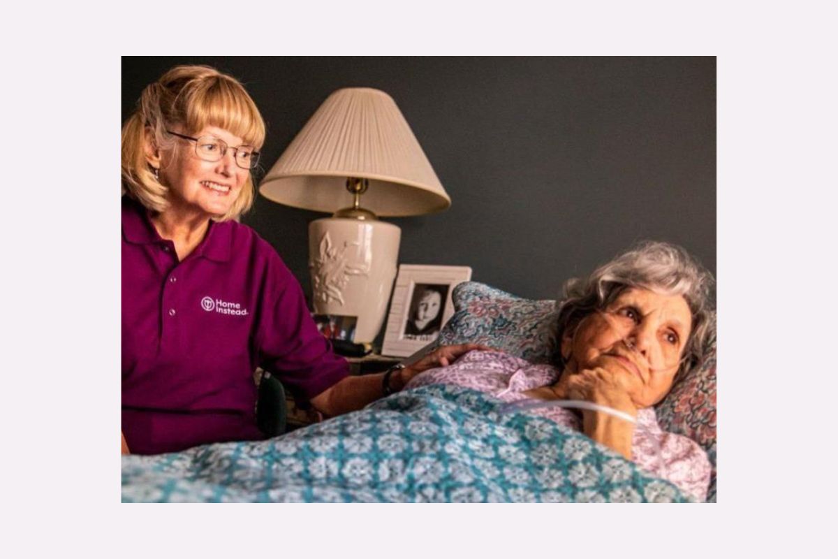 Home Instead Caregiver sitting next to a senior laying in bed