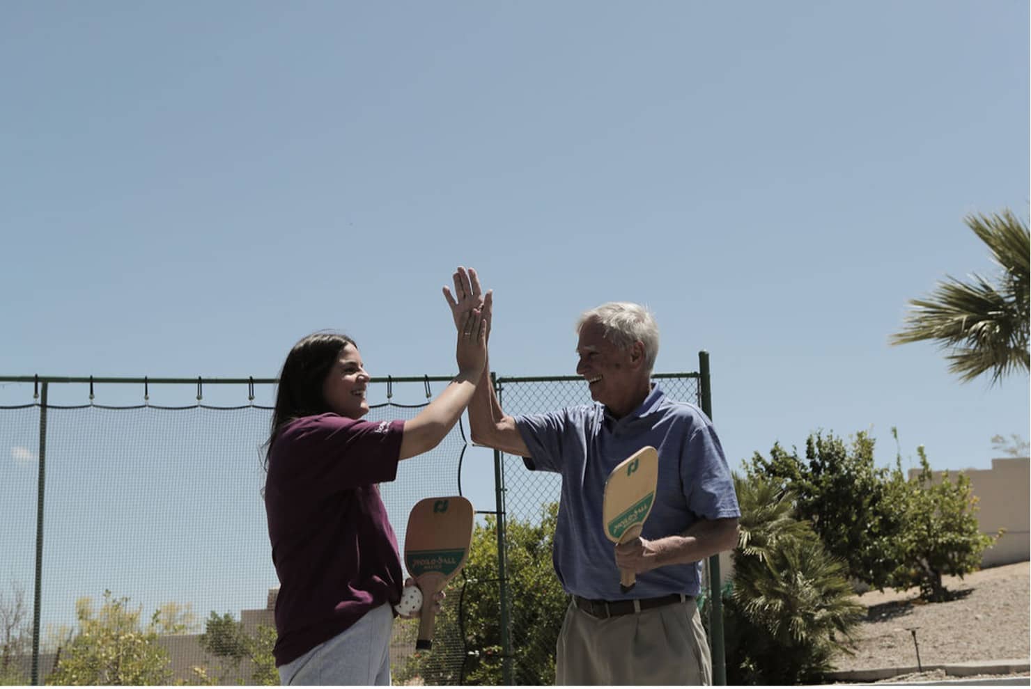 Photo of a family caregiver high fiving a senior at the pickle ball court