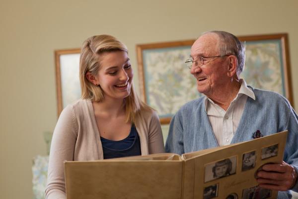 senior man and younger woman smile while reviewing photo album