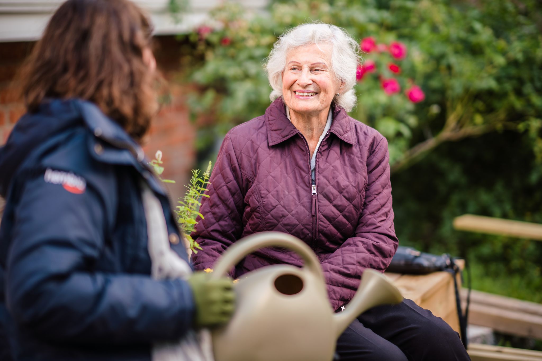 senior woman smiles while sitting outside with younger woman