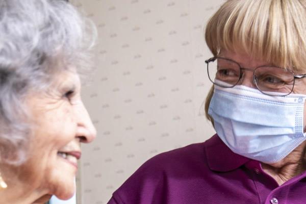 CarePro in a mask helping a senior through the hallway