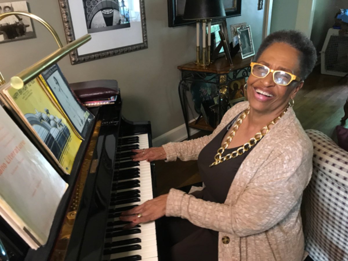 An aging woman smiling as she enjoys the piano at home.