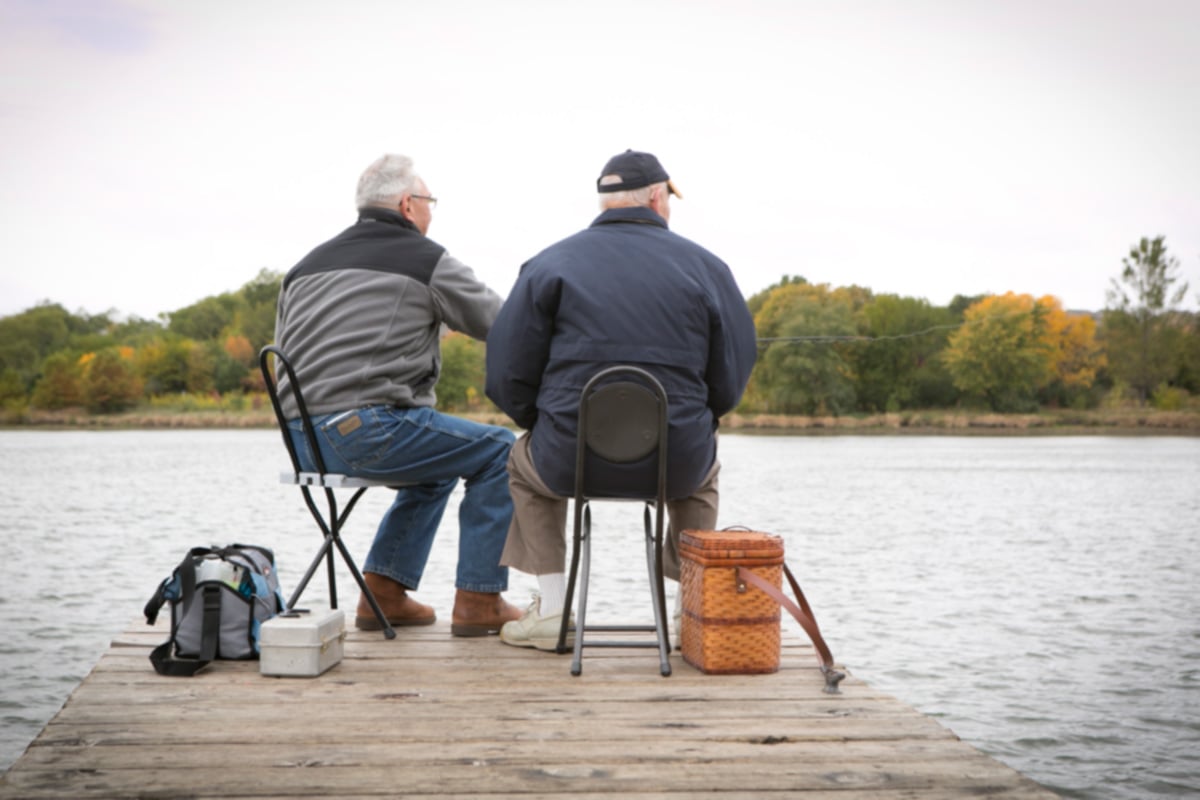 Senior man and son fishing together at the end of a dock