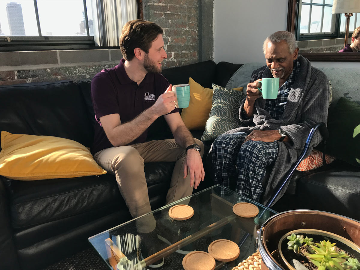 Home Instead Caregiver provides companionship to elderly man drinking coffee in his home.