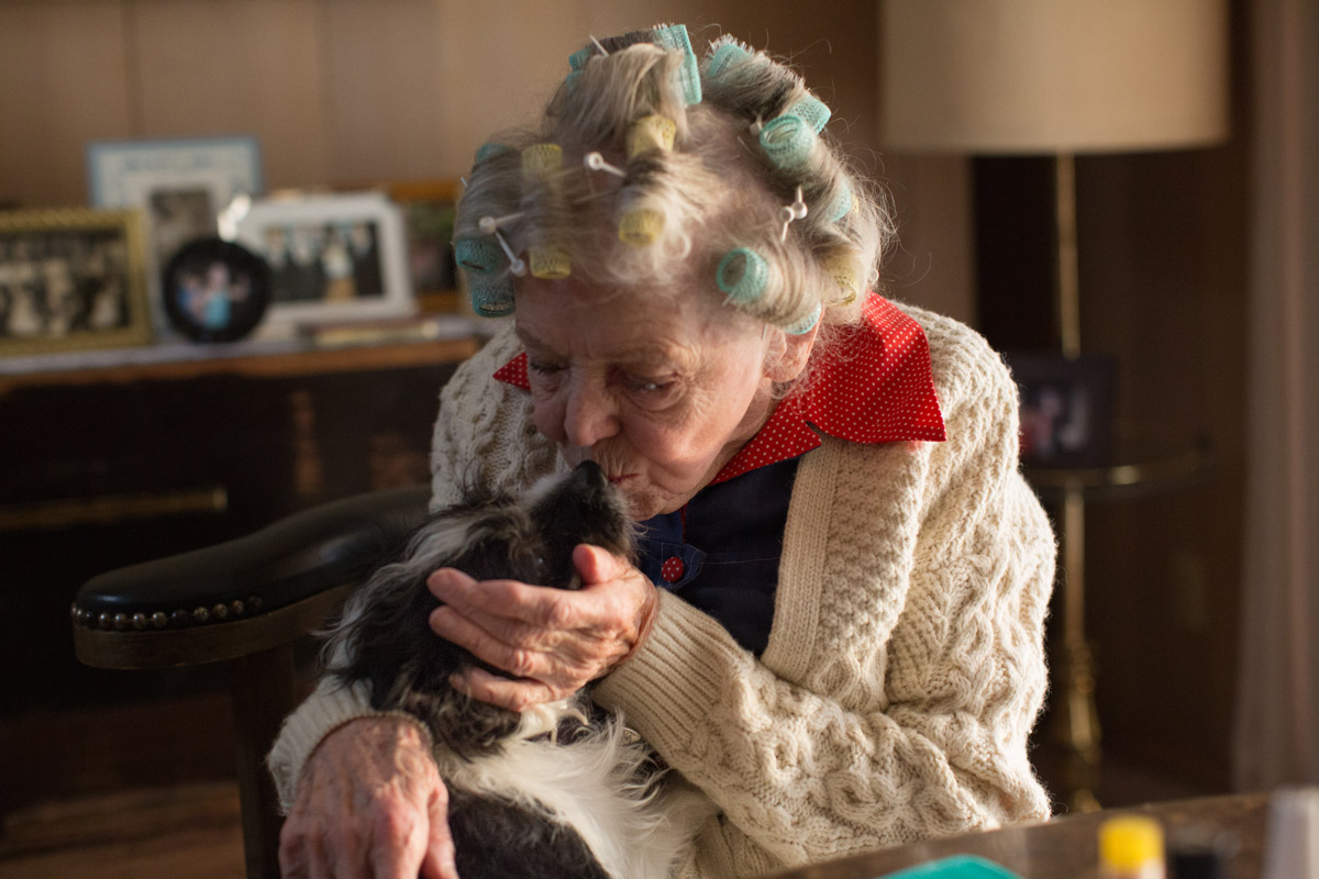 Elderly woman kissing her dog while sitting at home.