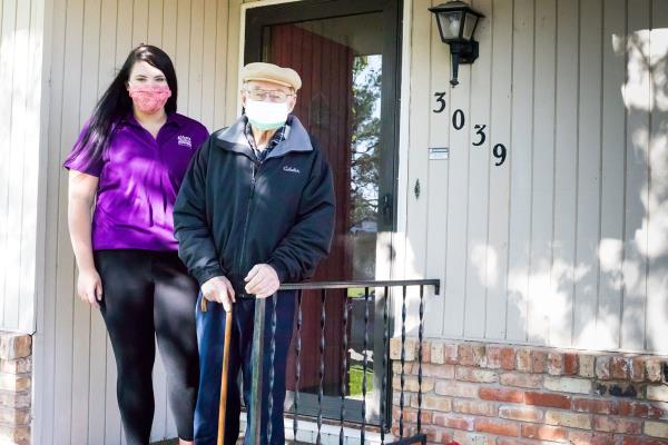 Home Instead Caregiver and senior client with cane stand on front porch wearing masks