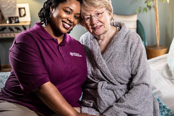 Home Instead CAREGiver and senior sitting on bed smiling