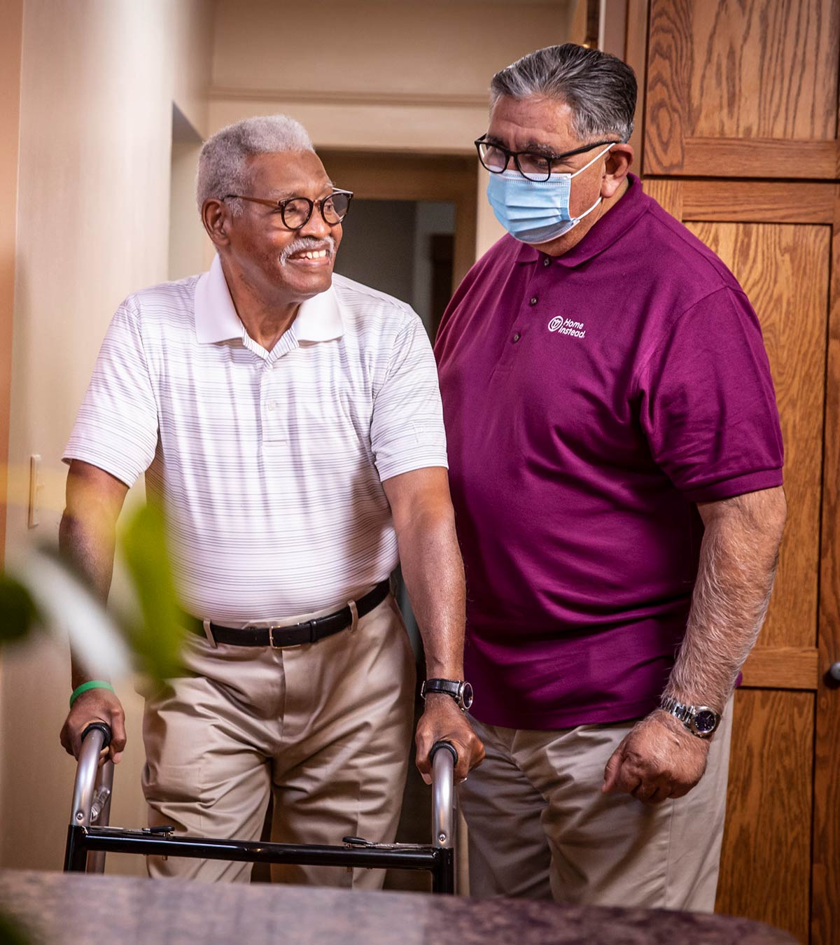Home Intead CAREGiver wearing a face mask helping a smiling senior using a walker