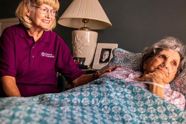 Home Instead CAREGiver sitting next to bed with senior