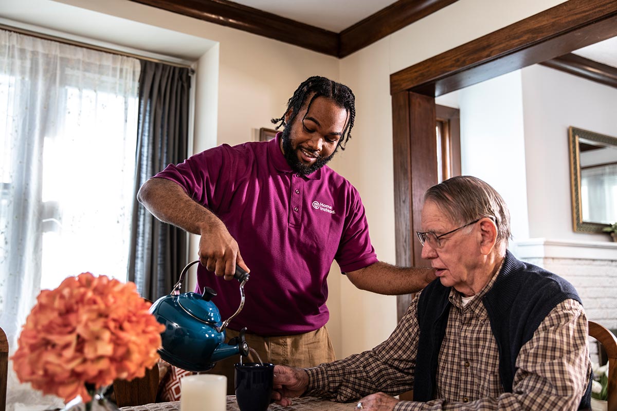 Home Instead CAREGiver pouring a cup of coffee for a senior man.