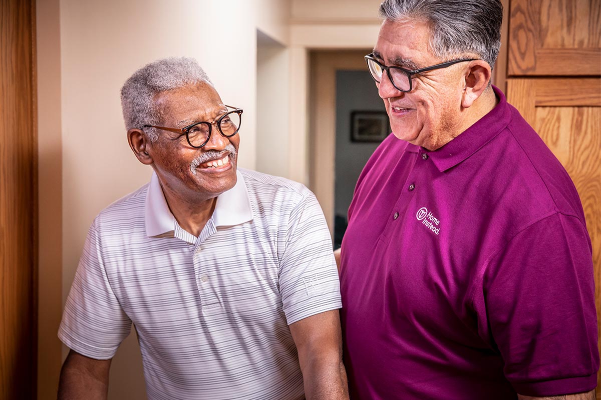 Home Instead Caregiver helps senior man walking at home and provides home care services near me