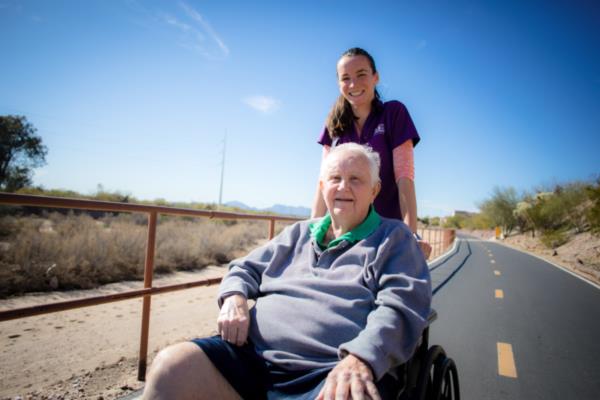 Home Instead Caregiver and aging man in wheelchair on a walk.