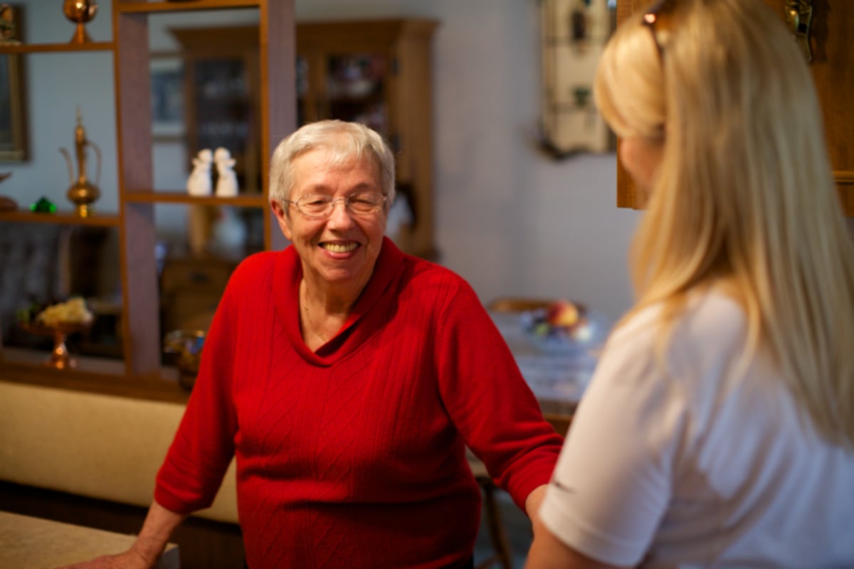 Home Instead Caregiver and aging woman talking and smiling at home.