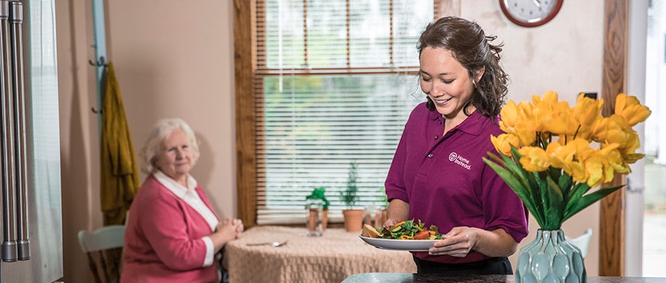 Home Instead Caregiver brings salad to senior woman at home