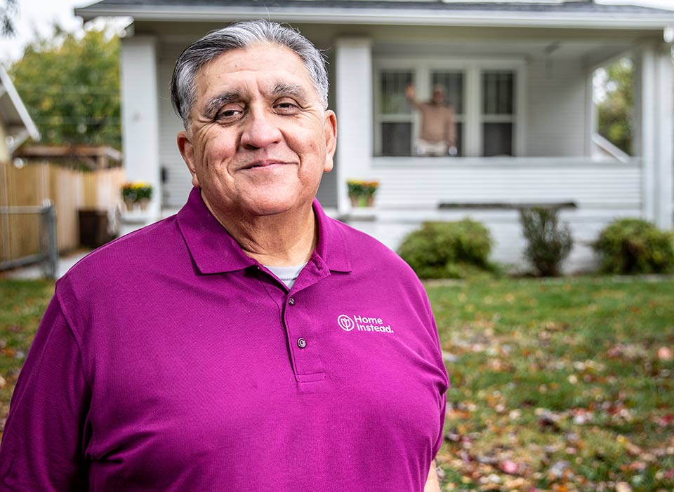 Home Instead Caregiver stands in front of house with senior waving from front porch