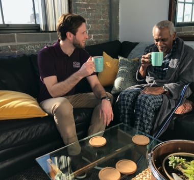 Home Instead Caregiver provides companionship to elderly man drinking coffee in his home.