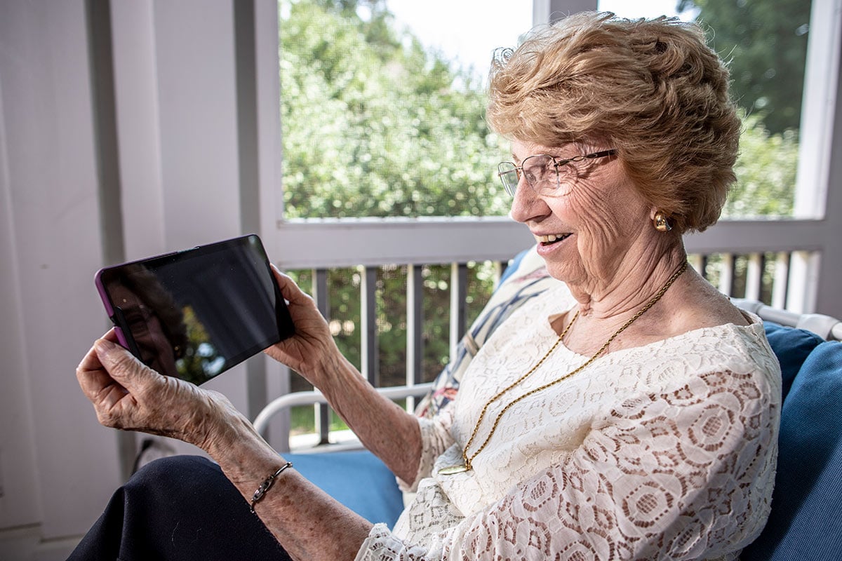 Senior woman smiling while reviewing resources on tablet at home