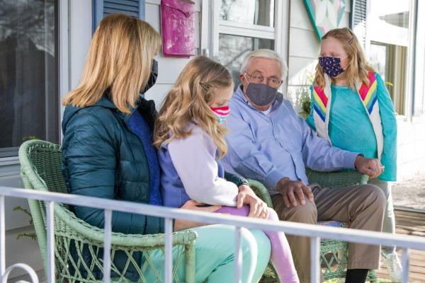 senior sitting with family on front porch wearing PPE